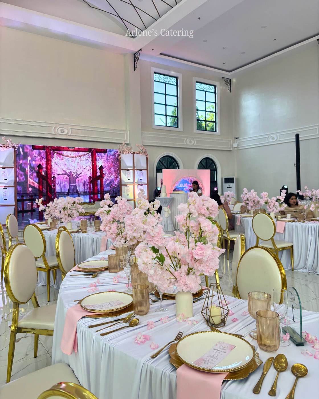 A full reception room styled with cherry blossom florals and pink uplighting